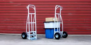 Two Richmond Australia hand trucks with stacked plastic bins and boxes in front of a red industrial shutter.